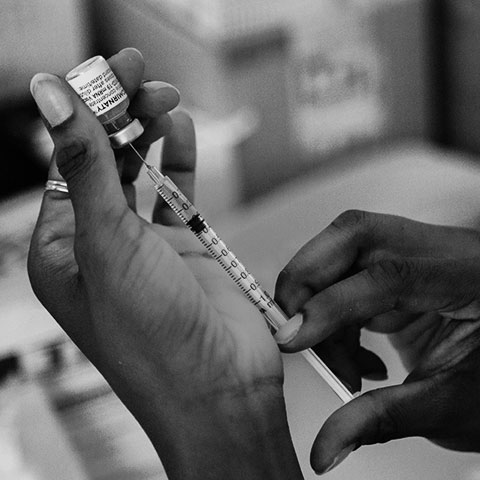 A black and white close-up of someone filling up a syringe from a vial