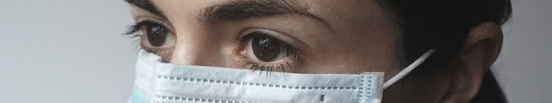 Close-up of a woman with dark features who is wearing a blue medical mask