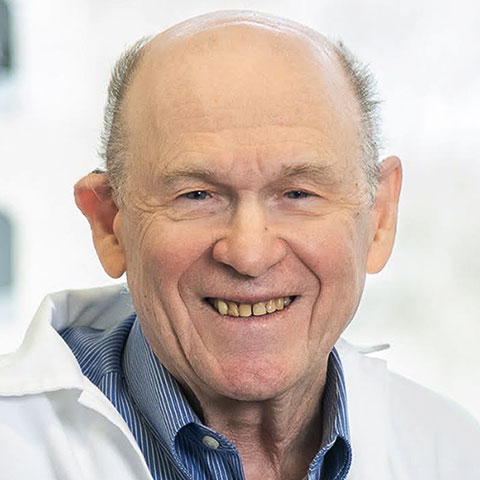 Close-up portrait of a smiling Dr. Nahum Sonenberg, who is wearing a white lab coat and a blue striped button-down shirt