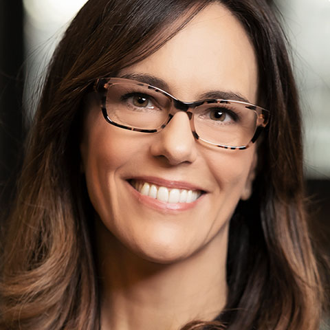 A close-up portrait of a smiling Prof. Amélie Quesnel-Vallée, who is wearing square-rimmed glasses