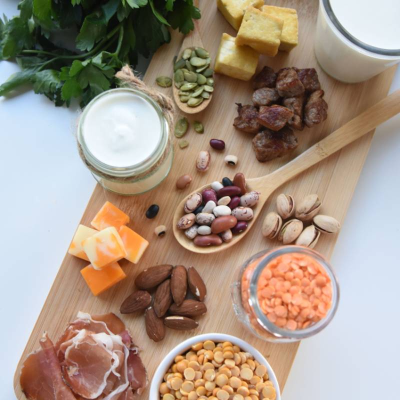 A spread of nuts, grains, beans, meat, and cheese placed on a wooden board